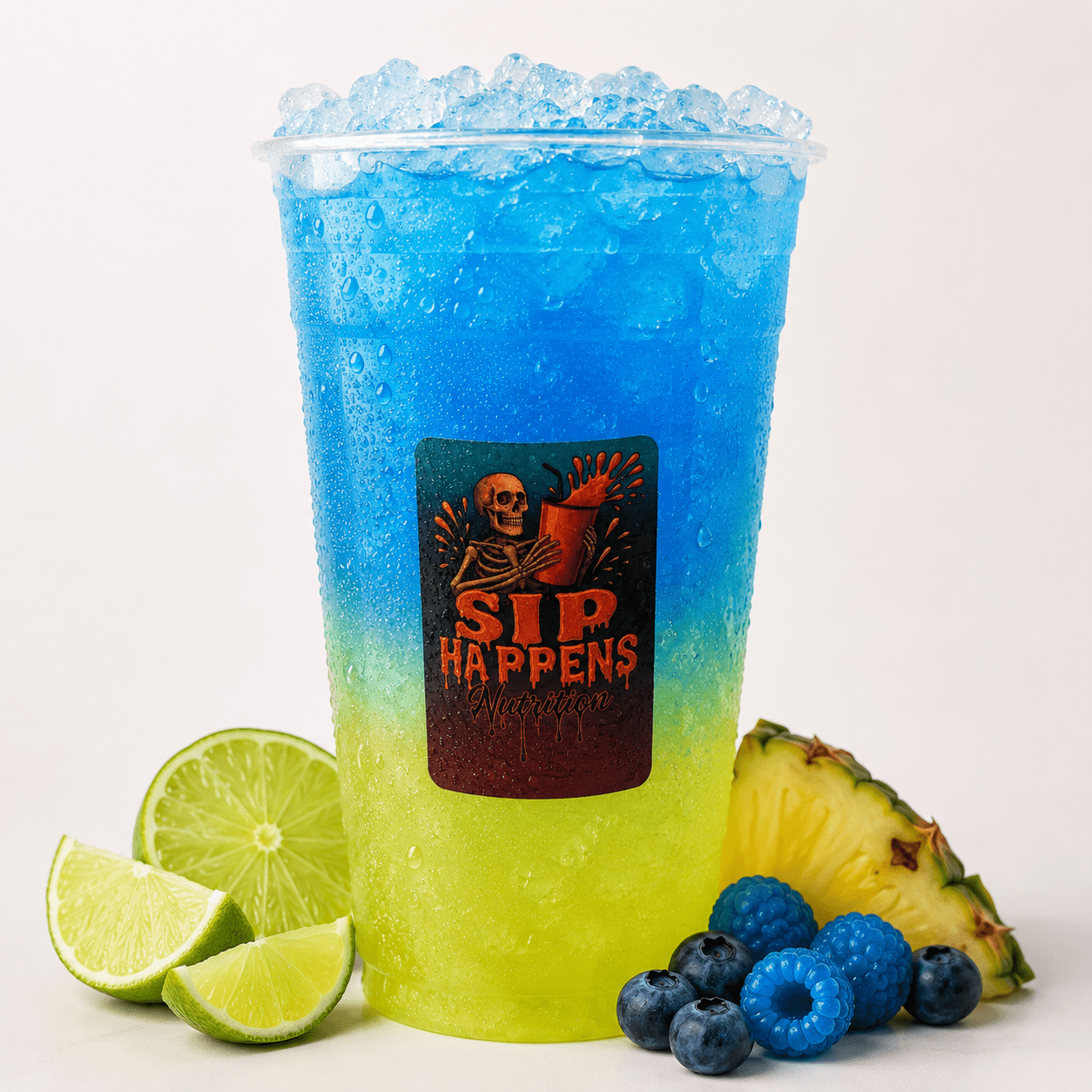 Sip Happens Nutrition iced drink with a yellow-to-blue gradient, surrounded by lime wedges, pineapple, blueberries, and blue raspberries