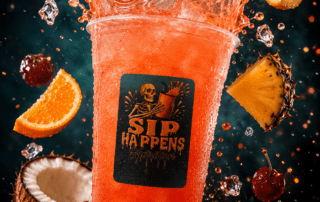 Sip Happens Nutrition red fruit drink in a clear cup surrounded by splashing liquid, cherries, orange slices, pineapple, and coconut