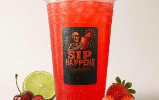 Sip Happens Nutrition red iced drink in a branded cup surrounded by fresh strawberries, cherries, and lime