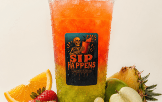 Sip Happens Nutrition iced drink with green-to-orange gradient, surrounded by fresh strawberries, orange slices, grapes, green apple, and pineapple