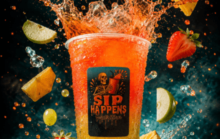 Sip Happens Nutrition drink cup with a vibrant orange-to-yellow gradient, surrounded by splashing liquid and fresh fruits including strawberries, oranges, pineapple, grapes, and lime