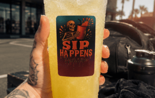 Tattooed hand holding a Sip Happens Nutrition iced drink outside Iron Fitness gym