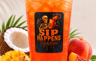 Sip Happens Nutrition iced orange drink in a branded cup surrounded by mango, cherries, peach, and coconut